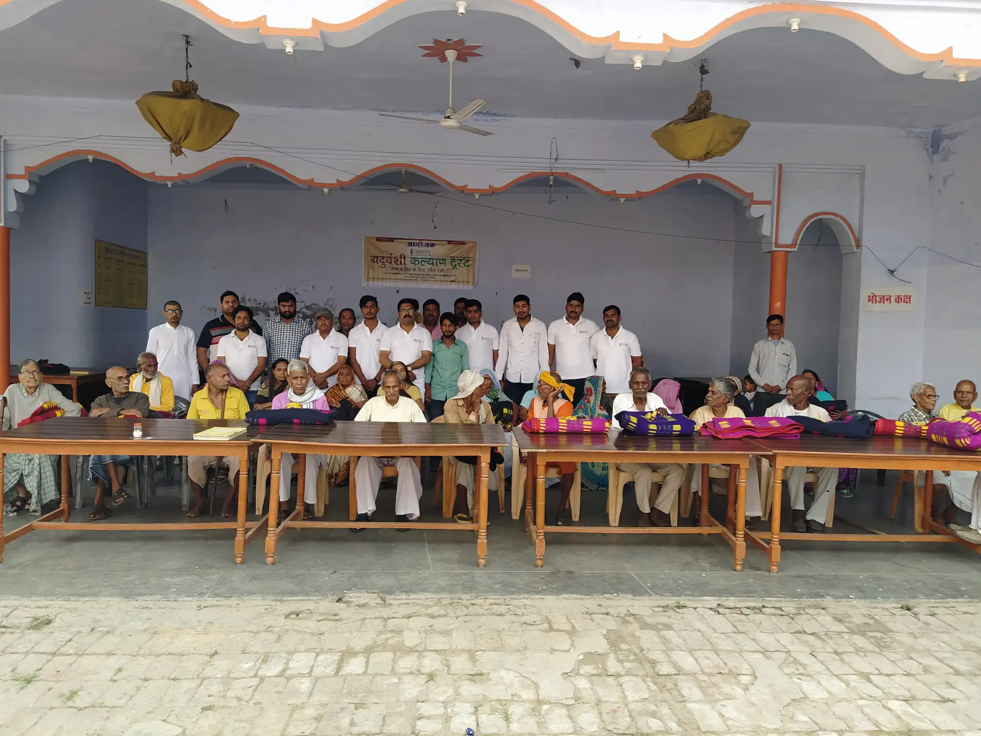 Trust members stand behind tables of blankets with elderly people seated in front