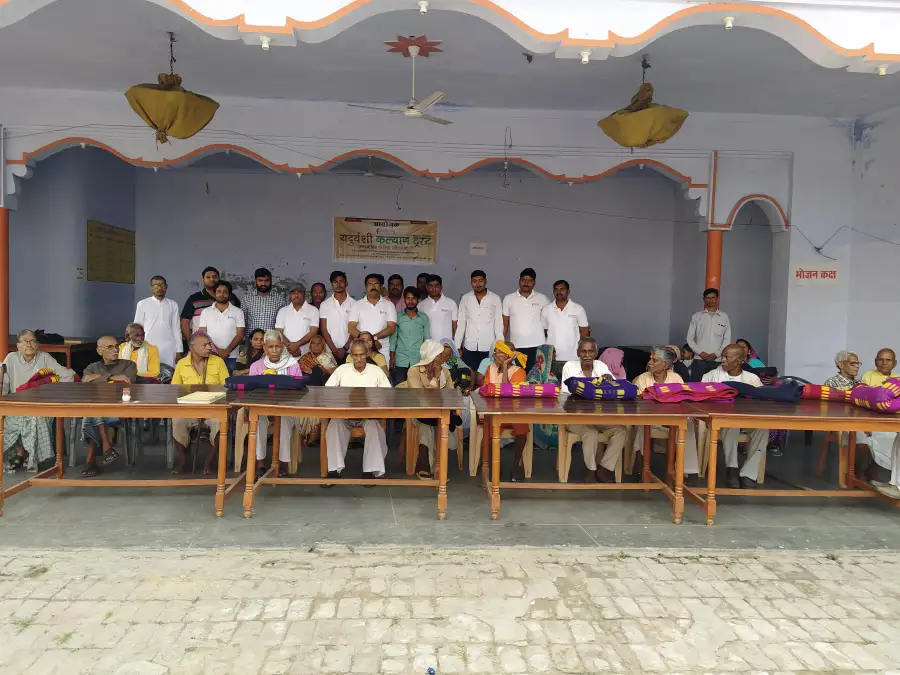Trust members stand behind tables of blankets with elderly people seated in front